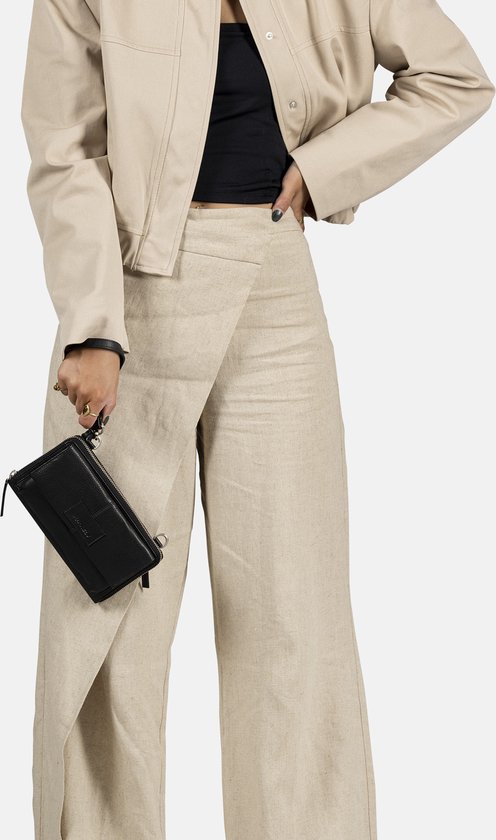 Zwarte croco-look telefoonportemonnee in de hand, gedragen door een model met beige jasje en wijde linnen broek.