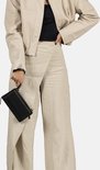Zwarte croco-look telefoonportemonnee in de hand, gedragen door een model met beige jasje en wijde linnen broek.