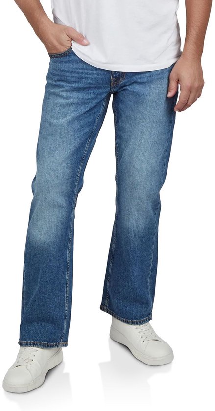 Man met de hand in de zak van een blauwe Mustang jeans, bootcut fit, met witte sneakers.