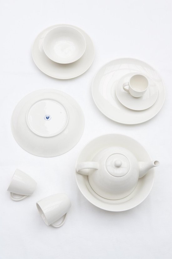 Wit porseleinen servies: theepot op schaal, stapels borden, mokken en een schaal, wit op wit.