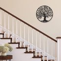 L'arbre de vie en métal noir est suspendu à un mur clair près d'un escalier avec une rampe brune.