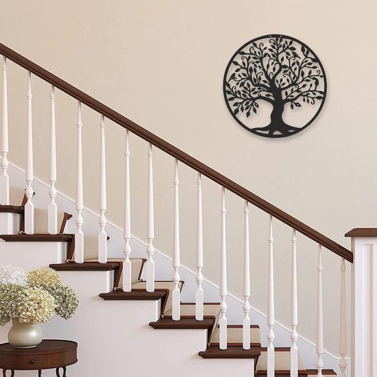 L'arbre de vie en métal noir est suspendu à un mur clair près d'un escalier avec une rampe brune.