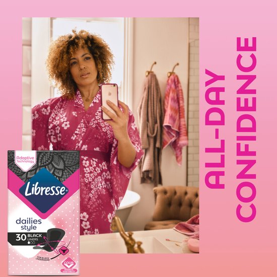 Vrouw in roze kimono in badkamer, bekijkt zichzelf in spiegel. Rechts een pak Libresse Dailies Style.