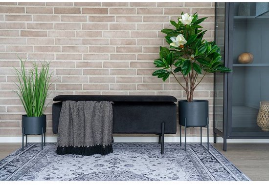 Zwarte fluwelen hocker met een gebreide plaid met franjes erop.