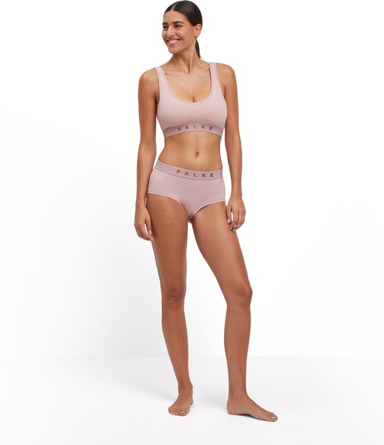 Een vrouw staat in een roze sportbeha en broek met FALKE-band.