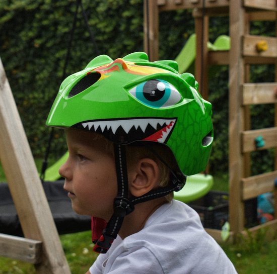 Kind met groene dinosaurushelm, witte tanden en grote blauwe ogen.