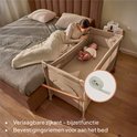 Lichtbruin reisbedje naast een bed, vastgemaakt met riemen. De verlaagbare zijkant is zichtbaar.