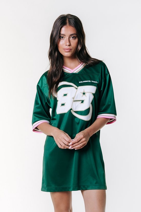 Mannequin portant une robe t-shirt de football verte, avec le numéro '85' en blanc et or, et des rayures roses, blanches et brunes sur le col et les manches.