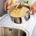 Afgieter van pasta in een roestvrijstalen pan met glazen deksel boven een gootsteen.