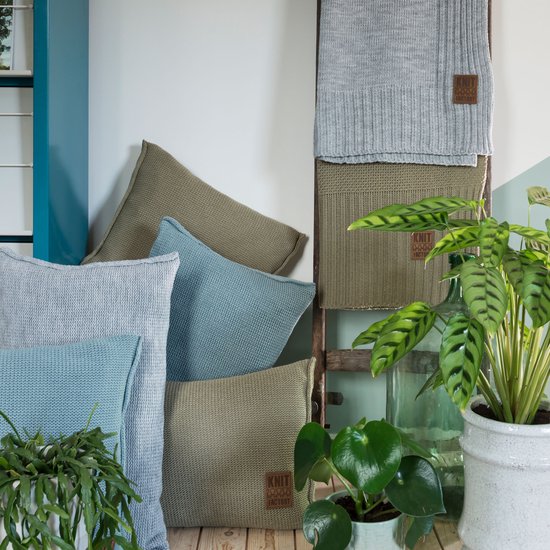 Lichtblauwe en groene kussens en een grijze plaid op een houten ladder, met planten.