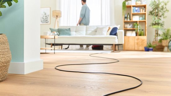Lange stroomkabel van rode Bosch stofzuiger die door een woonkamer loopt.