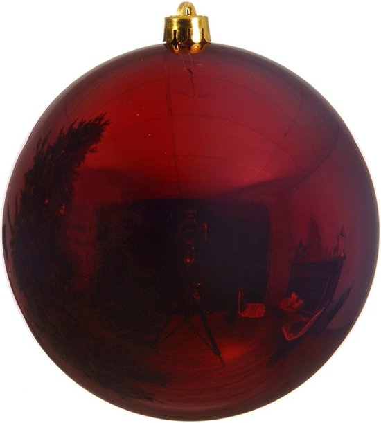 Boule de Noël rouge foncé brillante en plastique avec un capuchon doré. La boule reflète un sapin de Noël.