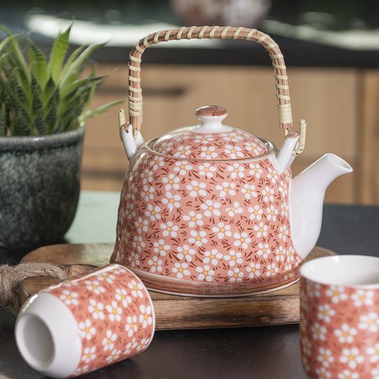 Roze theepot met witte bloemen, naast mokken.