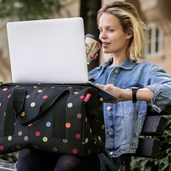Vrouw met sproeten en sproeten zit op een bankje met een laptop en een tas met stippen.