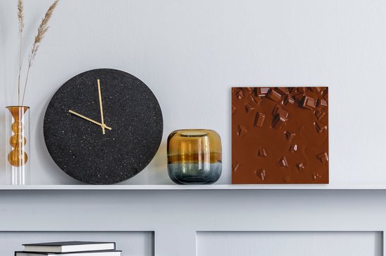 Gros plan de chocolat fondu avec des morceaux, sur une étagère murale à côté d'une grande horloge noire.