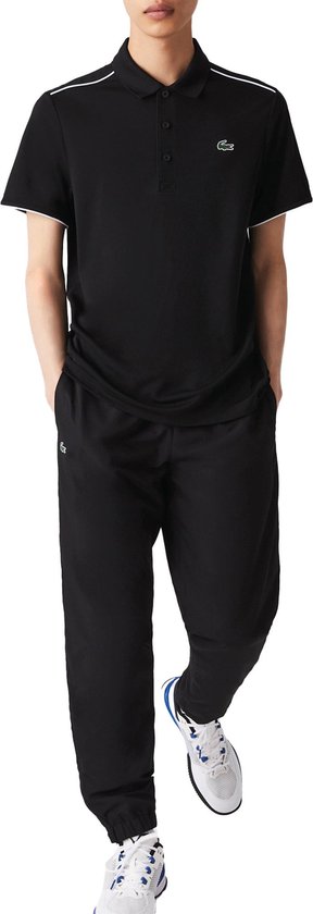 Model draagt een zwarte Lacoste poloshirt en bijpassende zwarte trainingsbroek met witte accenten.