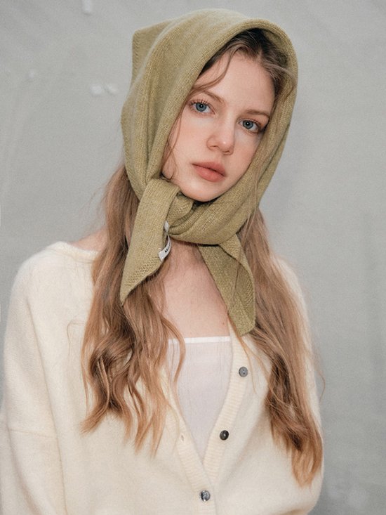 Model draagt een gebreide gebroken witte vest. De olijfgroene sjaal wordt als hoofddoek gedragen met de uiteinden geknoopt.