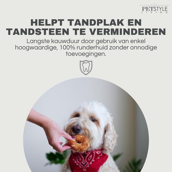 Een hand houdt een ringvormige hondensnack voor een hond met een rood bandana.