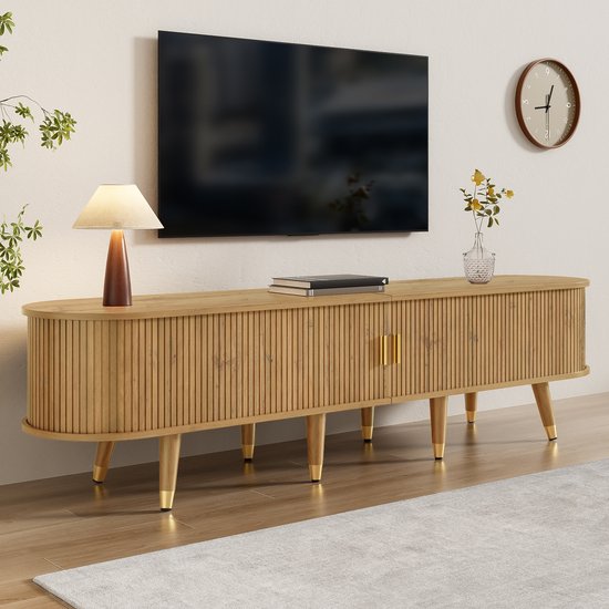 Houten tv-meubel met verticale ribbels, twee gouden handgrepen, gouden poten en is ingericht met een tv, lamp en plant.