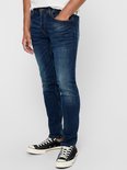 Man in donkerblauwe skinny jeans met lichte slijtage en zwarte sneakers met witte veters.