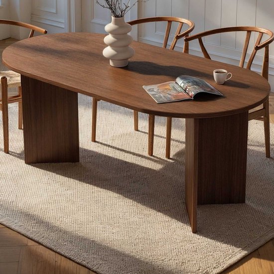 Ovale eettafel van donker hout met twee verticale poten, met daarop een vaas en een tijdschrift.