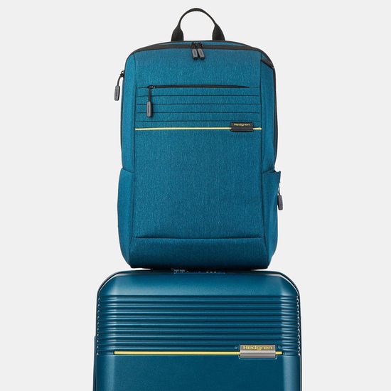 Blauwe Hedgren laptoprugzak met gele accenten, bovenop een blauwe koffer.
