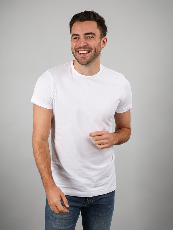 Model glimlacht en draagt een wit katoenen T-shirt met ronde hals en korte mouwen, gecombineerd met een spijkerbroek.