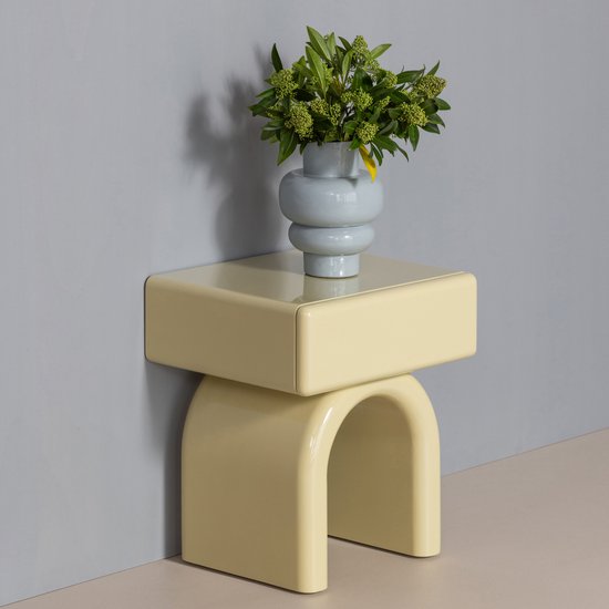 Gele bijzettafel met boogpoot en rechthoekig blad, versierd met een vaas met groene takken.