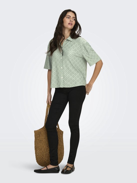 Model met lichtgroene blouse met broderie anglaise, zwarte skinny jeans en tas.