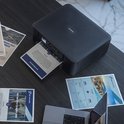 Zwarte Brother printer op een donker bureau, papier wordt uit de printer gevoerd, met documenten eromheen.