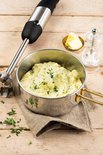 Fritel staafmixer naast een pot aardappelpuree met gesmolten boter en pepermolen.