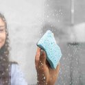 Une femme lave une porte de douche en verre avec une éponge à récurer bleue.