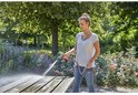 Vrouw sproeit een houten picknicktafel in een tuin met een Gardena spuitpistool.