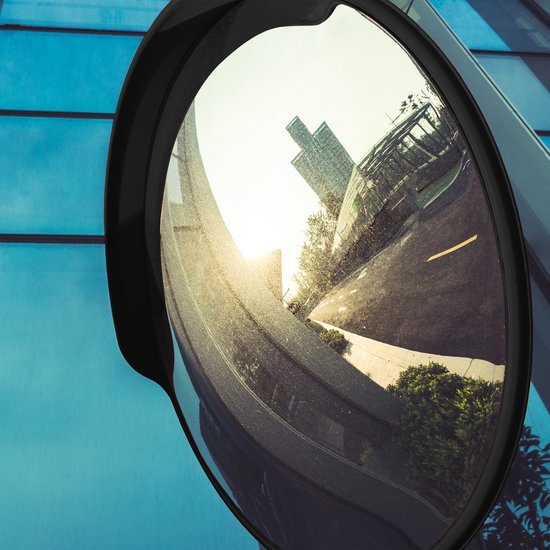 Bâtiments et parking reflétés dans un miroir rond et convexe à bord noir, sur une façade en verre bleue.