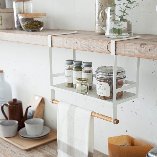 Étagère à épices blanche suspendue avec barre porte-serviettes en bois, garnie de petits pots et d'un grand bocal en verre.