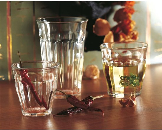 Trois verres Duralex, un rempli de boisson jaune. Deux verres vides avec des piments rouges séchés.