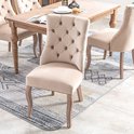 Beige fluwelen eetkamerstoel met knopen-quilting en gebogen houten poten op een vloerkleed.