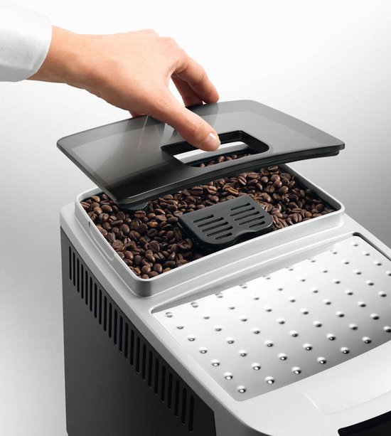Hand sluit deksel van de zilverkleurige volautomaat, gevuld met koffiebonen.