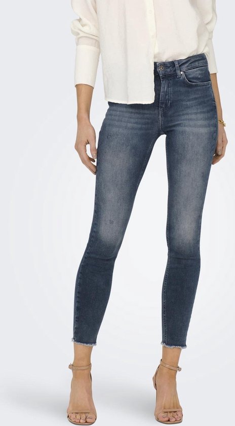 Vrouw met een wit shirt en een donkerblauwe skinny jeans met rafelige zoom, met beige sandalen met bandjes.