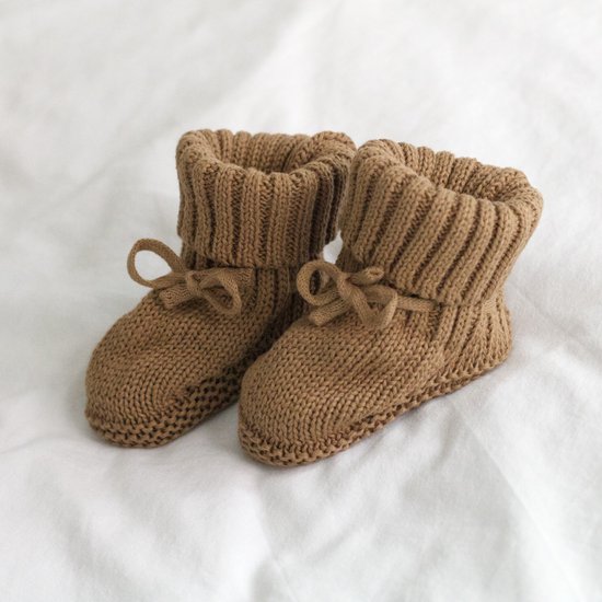 Bruine gebreide babyslofjes met omslagboord en strikje, op een witte achtergrond.