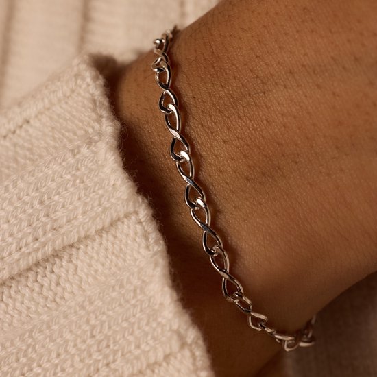 Close-up van een zilveren infinity schakelarmband op een vrouwenpols.