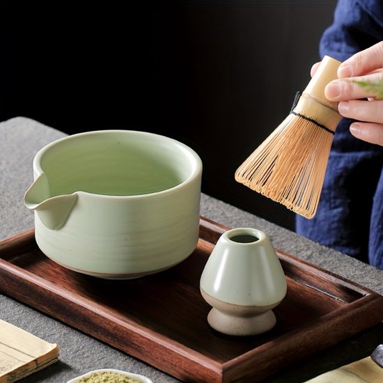 Handen die een groene matcha kom en blauwe houder schoonmaken met een bamboe klopper.