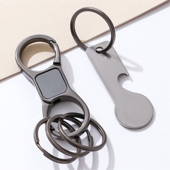Donker metalen karabijnhaak sleutelhanger en zilverkleurige flesopener met winkelwagenmunt, op witte achtergrond.