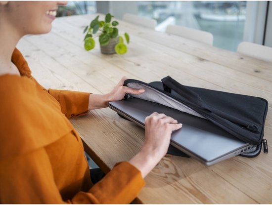 Een vrouw met een oranje blouse plaatst een laptop in een zwarte laptoptas.