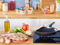 Een zwarte koekenpan met een houten spatel staat op een gasfornuis. Ingrediënten voor een ontbijt liggen ernaast.