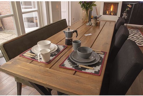 Grijze serviesjes met mokken, borden en kommen op een houten tafel, gedekt voor een maaltijd.
