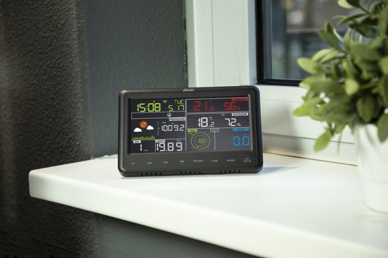 Zwart Alecto display op een witte vensterbank, toont tijd, datum, temperatuur, druk, wind en regen.