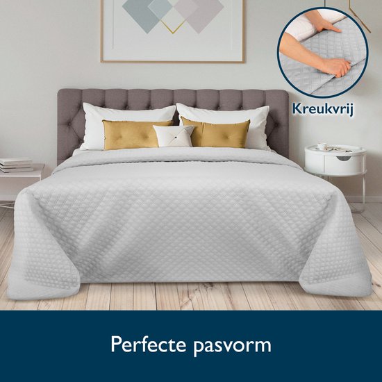 Grijze sprei met ruitpatroon op een bed met gestoffeerd hoofdbord. Kreukvrij.