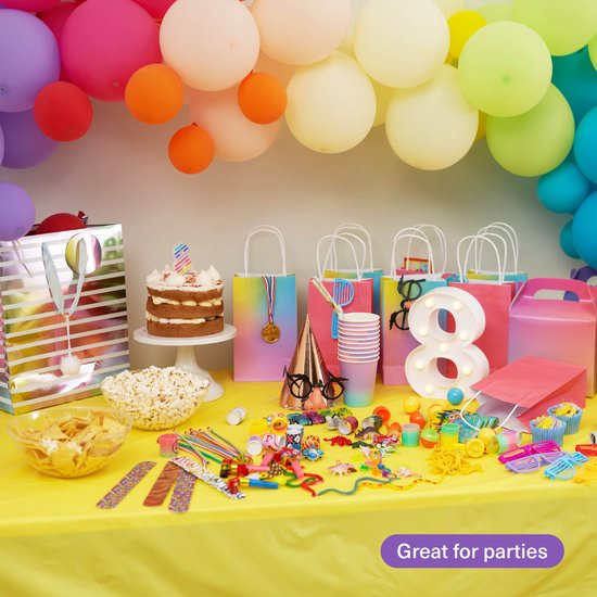 Een lange tafel vol met feestartikelen, waaronder een taart, popcorn, geschenken en ballonnen.
