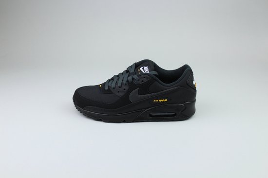 Zwarte Nike Air Max 90 sneaker met gele 'AIR MAX' opdruk op een grijze achtergrond.